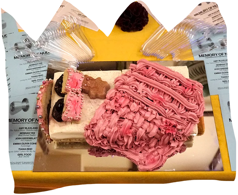 A cake decorated to look like a bed with ornate pink icing sits on top of a table covered in printed materials