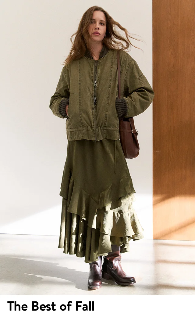 A woman wearing a green bomber jacket and ruffle maxi skirt with brown boots and a brown handbag.