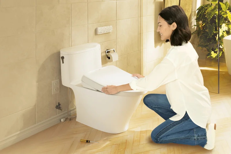 A woman easily installs a WASHLET bidet seat in a sunlit bathroom with decorative plant accents