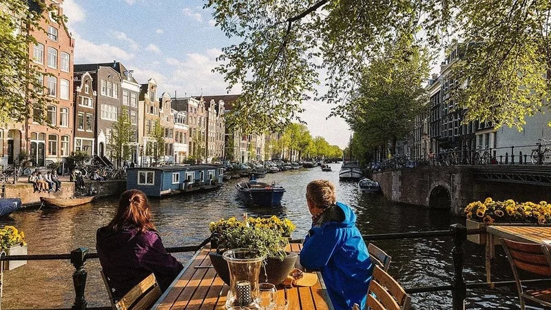 Image description: Couple sitting at table looking at canal in Amsterdam.