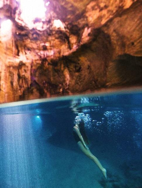 Image Description: A traveler swimming in the Thunderball Grotto cave in the Bahamas