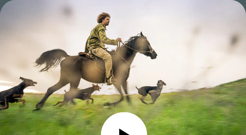 A man on horseback gallops while his pack of dogs run alongside him.