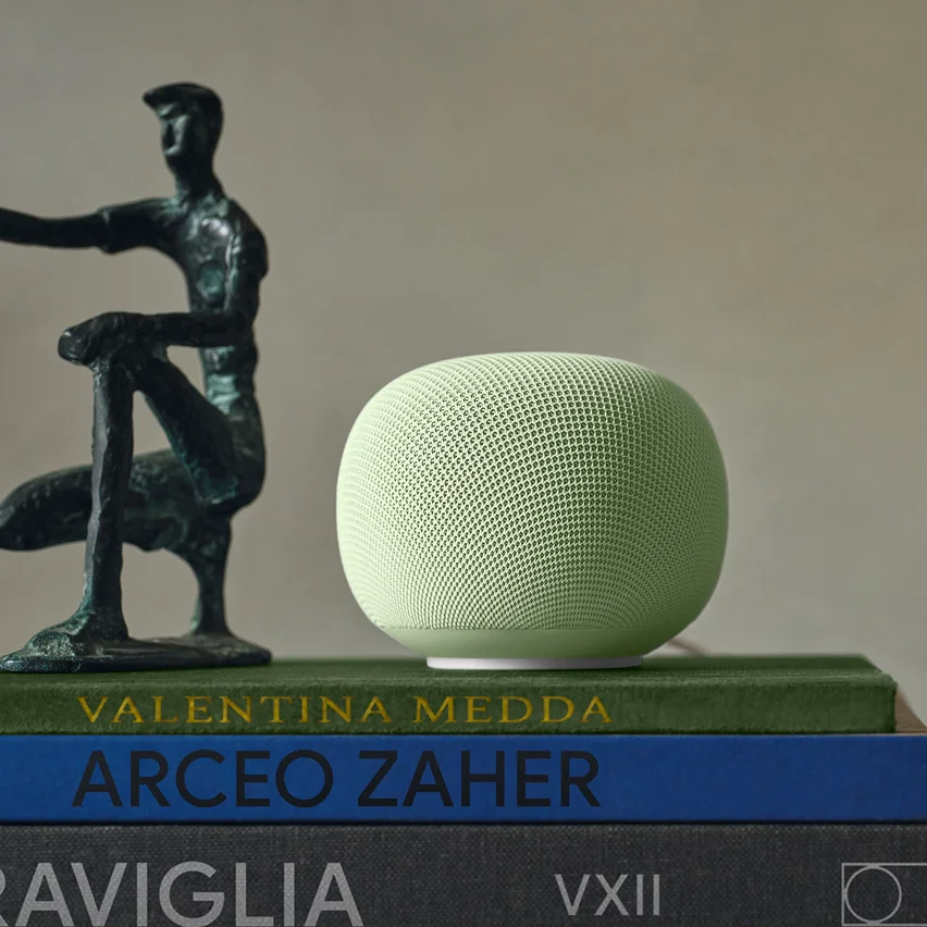 Green smart speaker on a stack of books beside a bronze abstract sculpture.