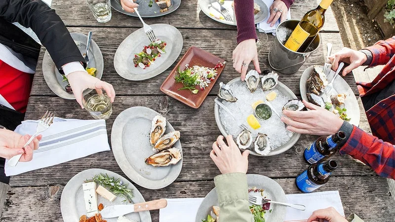 Image description: Overhead view of friends enjoying oysters and seafood at Hog Island Oyster Company’s Boat Oyster Bar in Marshall, CA