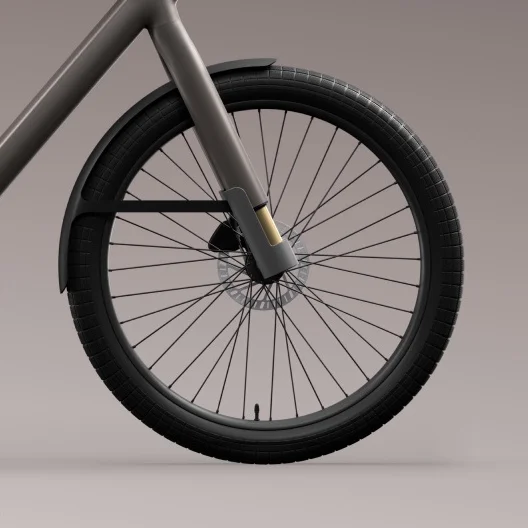 A detailed view of the front wheel of a Cowboy e-bike, showing its thick black tyre, mudguard, and suspension fork with a gold accent on the inner fork tubes.