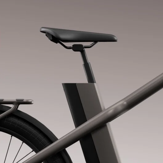 A close-up of the rear seat post and part of the rear wheel of a Cowboy e-bike in a sleek grey finish. The bike’s battery is visible integrated into the frame, and the rear carrier rack is partially seen.