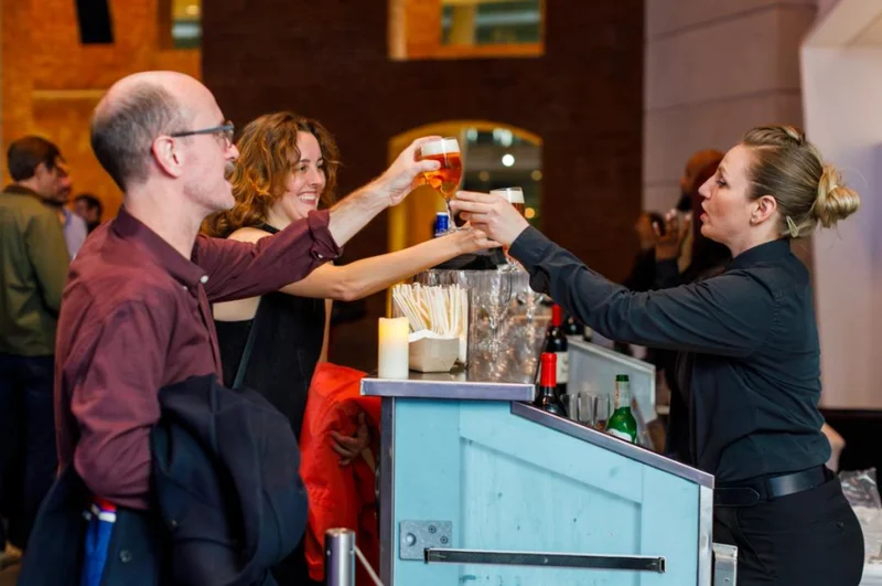 A bartender handing two people drinks