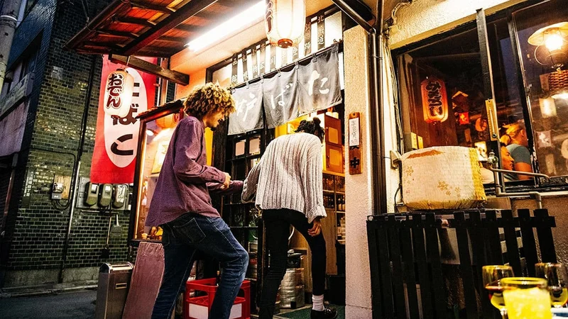 Image description: Two friends walking into bar in Tokyo