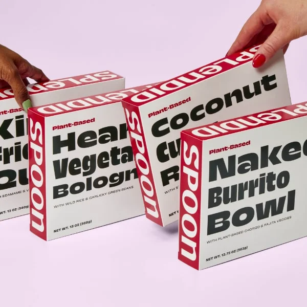 4 boxes of Splendid Spoon Dishes on a pink background. A hand reaches in from left and right, beginning to pick up two of the boxes