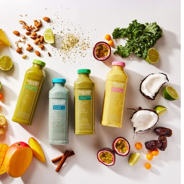 4 Splendid Spoon Smoothies laying on a white background, surrounded by some of our ingredients: fruits, veggies, nuts and spices.