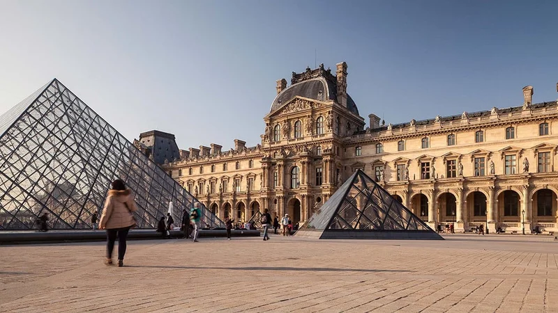 Image description: Woman walking outside of Louvre Museum in Paris