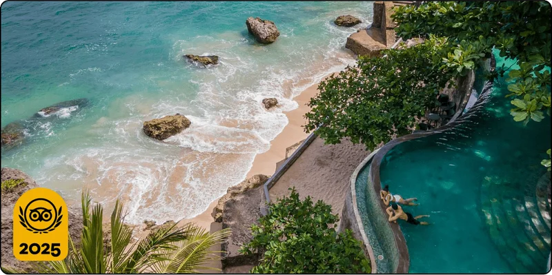Image Description: Aerial shot of a couple at the edge of an infinity pool that overlooks a secluded beach with rocks and trees.