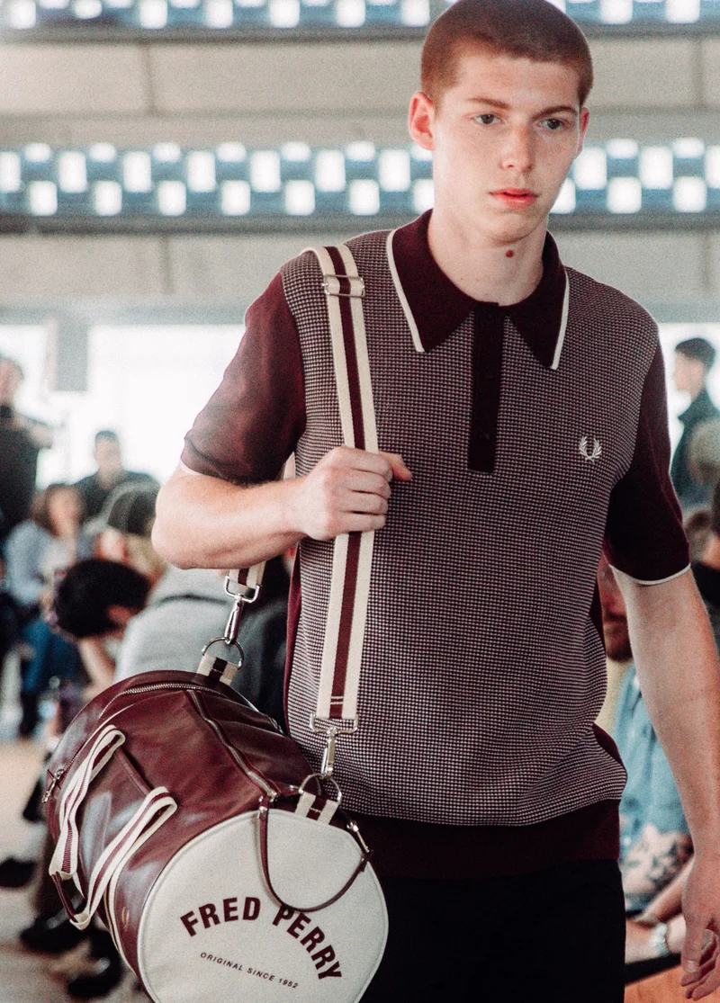 Male model wearing a Tonic Waffle Knitted Shirt in Oxblood carrying a Fred Perry Barrel Bag in Oxblood