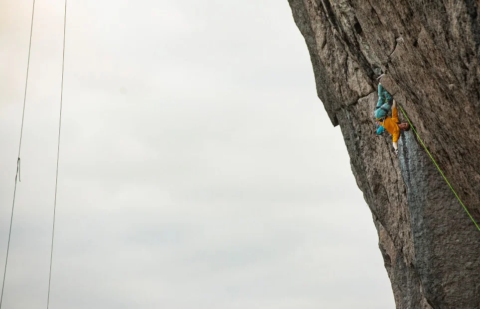 A climber hangs upside down on an overhanging rock wall.