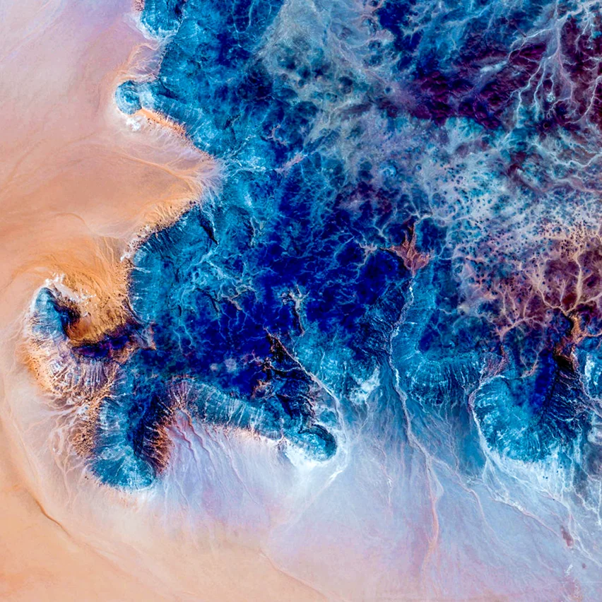 An abstract, aerial-view image showing a contrast between sandy-colored terrain and a rich, textured blue mineral formation.