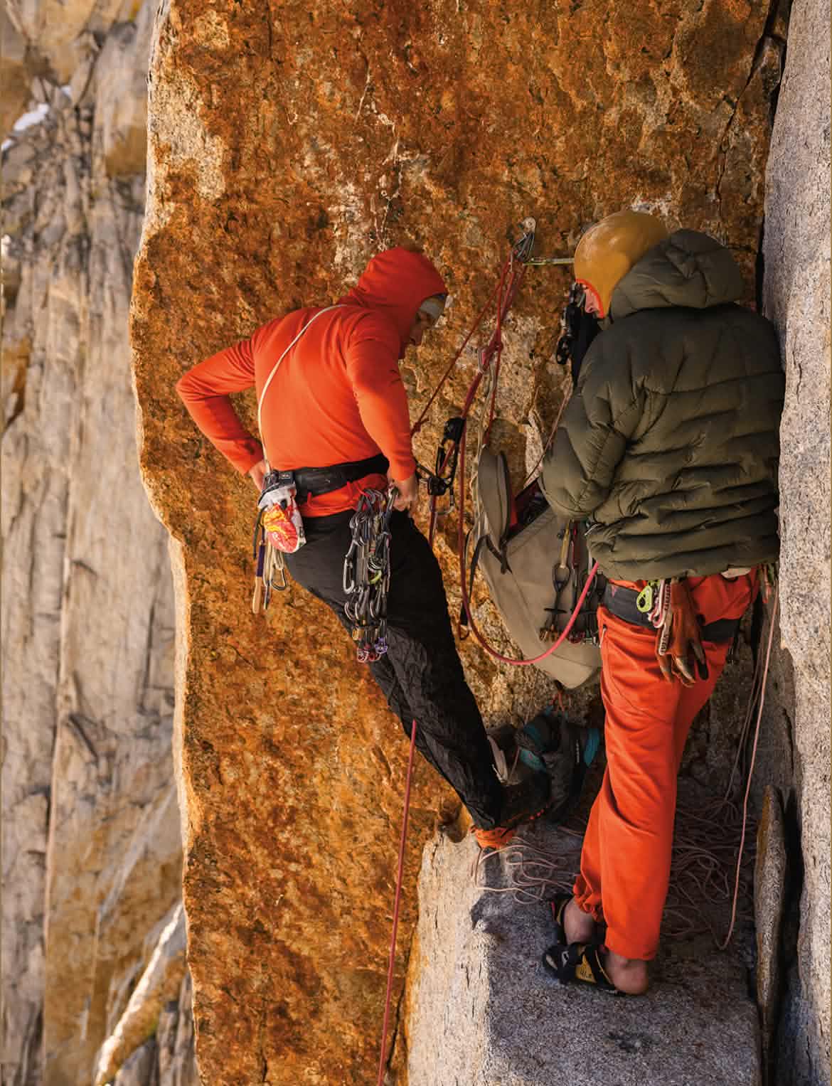 Two climbers swap leads on a belay ledge.