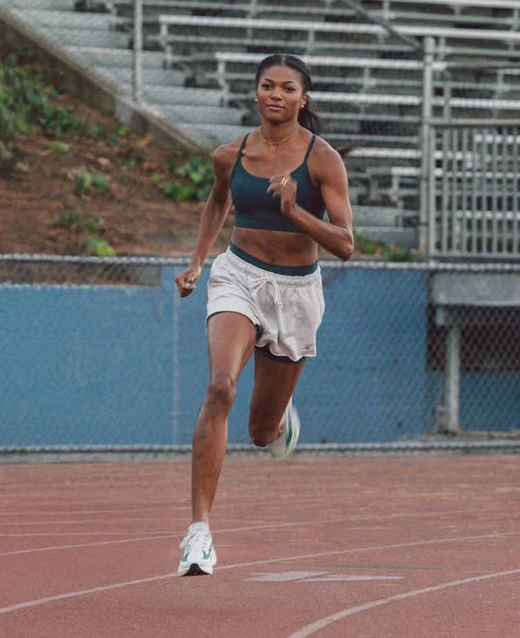 A young and fit female runner trains in a dark teal sports top and white running shorts with a matching dark teal band at the waist.