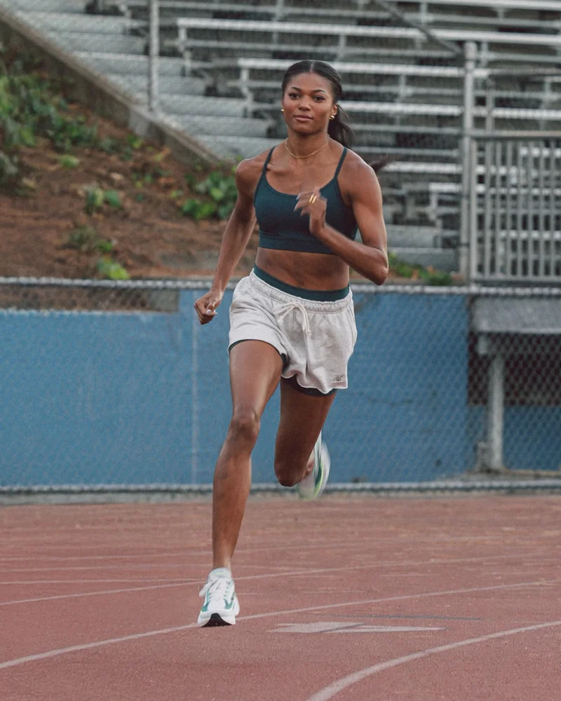A young and fit female runner trains in a dark teal sports top and white running shorts with a matching dark teal band at the waist.