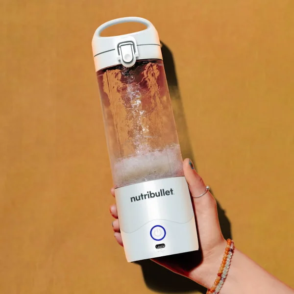 Hand holding a white nutribullet Portable Blender filled with water.