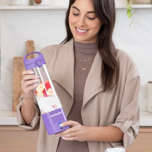 Woman smiling while holding a purple nutribullet Portable Blender filled with milk and fruits.