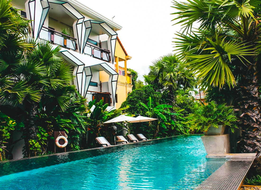 Image Description: Long, rectangular pool surrounded by tropical plants with 3D geometric architecture lining the outside of the hotel building.