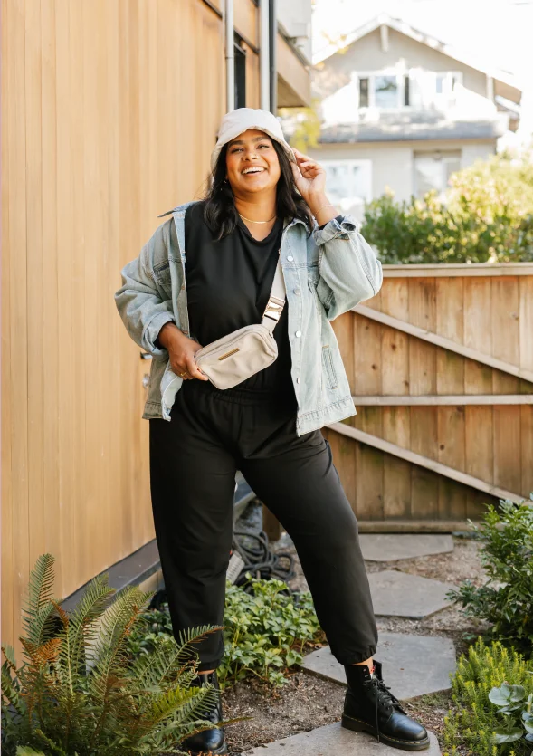 woman in garden wearing black romper, cream belt bag and denim jacket