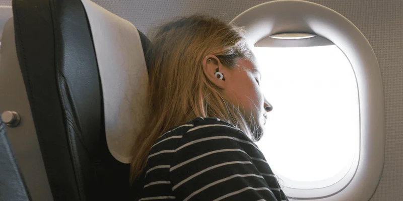 A woman wearing Loop earplugs sleeps on an airplane.