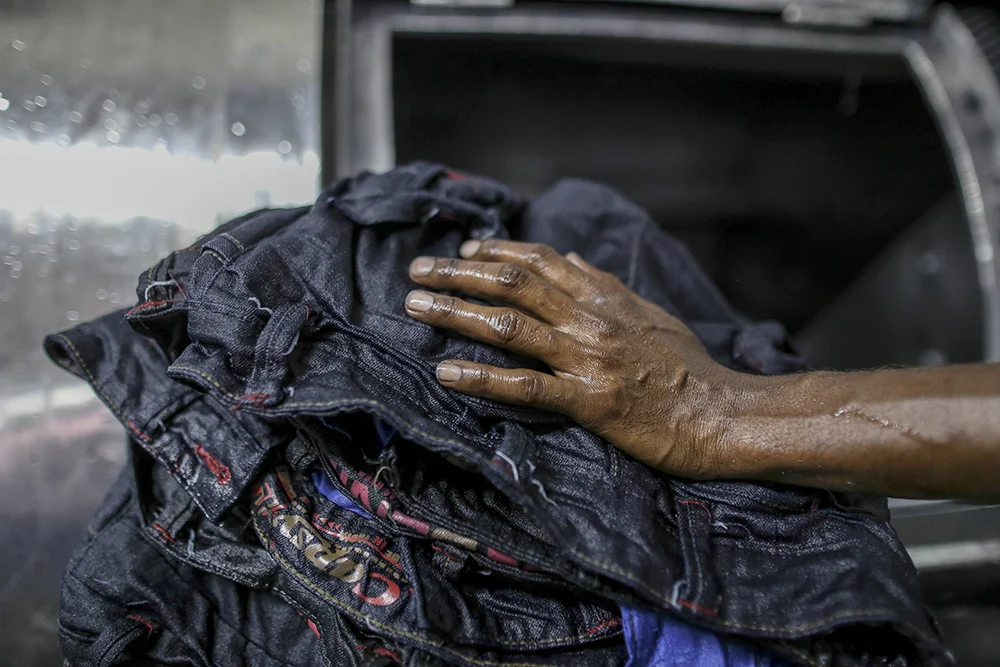 The hand of a worker unloading jeans from a fabric dyeing machine at a factory