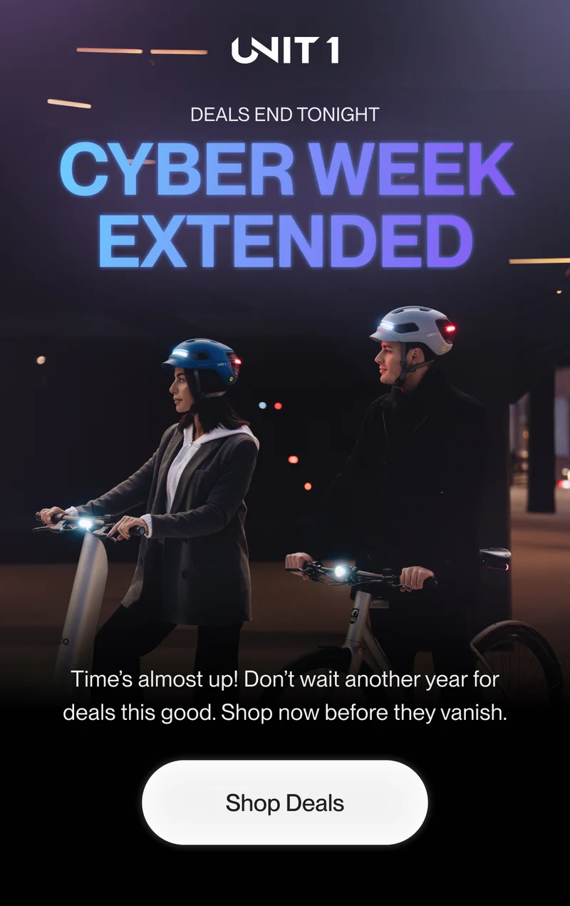 Two cyclists wearing UNIT 1 smart helmets with glowing front and rear lights, riding in a dimly lit urban environment. Overlay text reads 'Cyber Week Extended - Deals End Tonight' in bright blue and purple lettering.