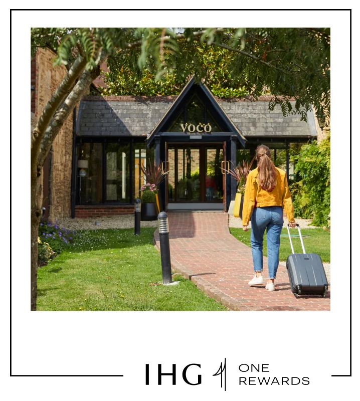 A woman entering a charming voco hotel entrance with her suitcase.
