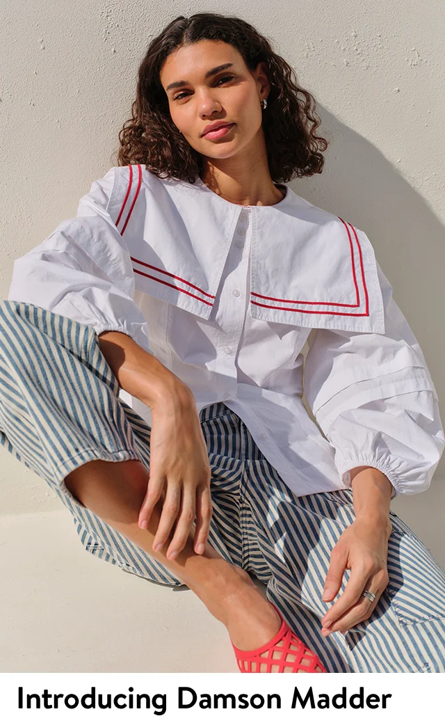 A woman wearing a white blouse with red piping and blue striped pants.