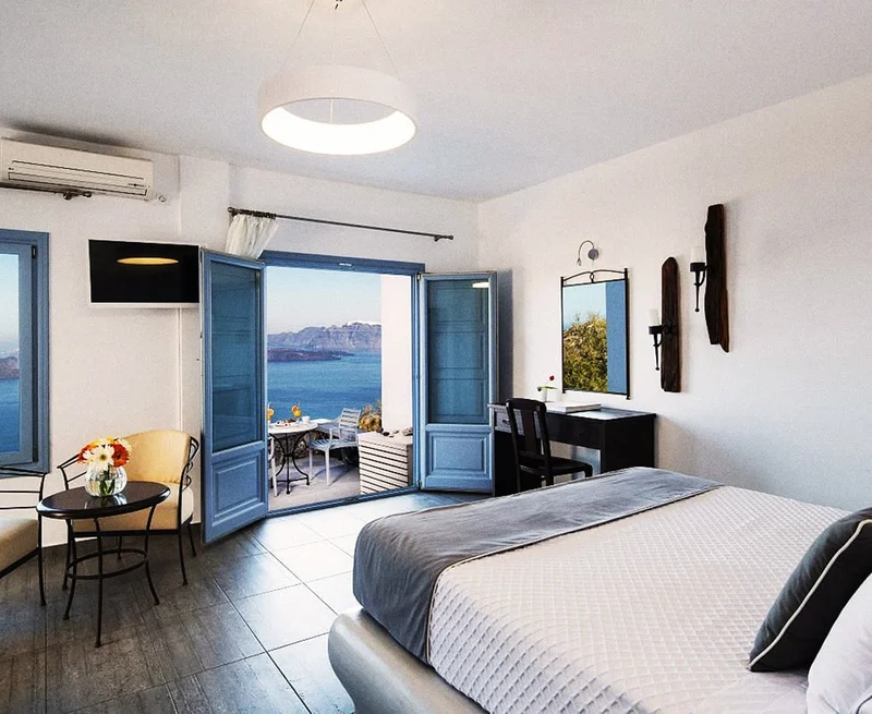 Image Description: A bed in a blue and white hotel room. A double door with blue shutters opens to a patio that has a table and chairs and a view of the sea.