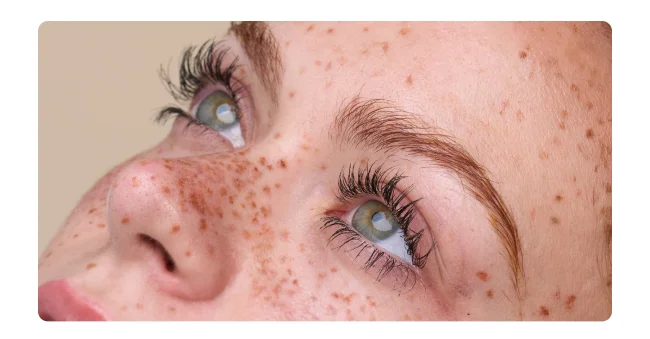 Close-up of natural-looking enhanced eyelashes and brows on person with freckles and green eyes