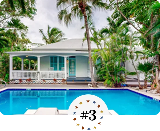 Charming coastal cottage with wraparound porch, lush palms, and inviting pool.