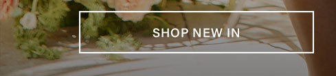 Softly blurred image of pale pink and white flowers with lush green foliage and sunlit shadows. White button reads "SHOP NEW IN" to discover the new collection.