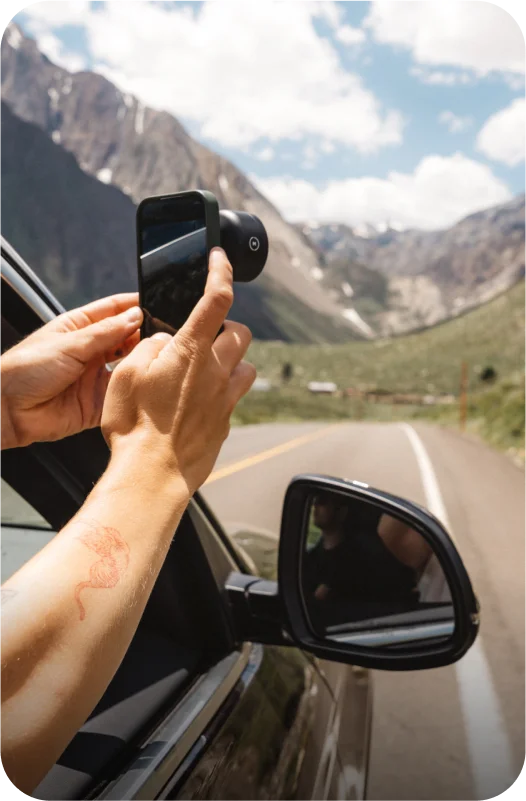 person holding phone out a car window with a moment lens attached