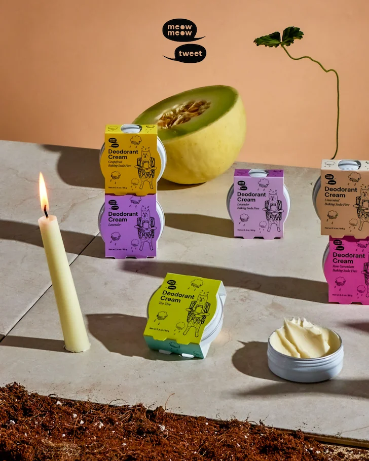 A collection of deodorant creams arranged with a tipping lit candle and a cantalope.