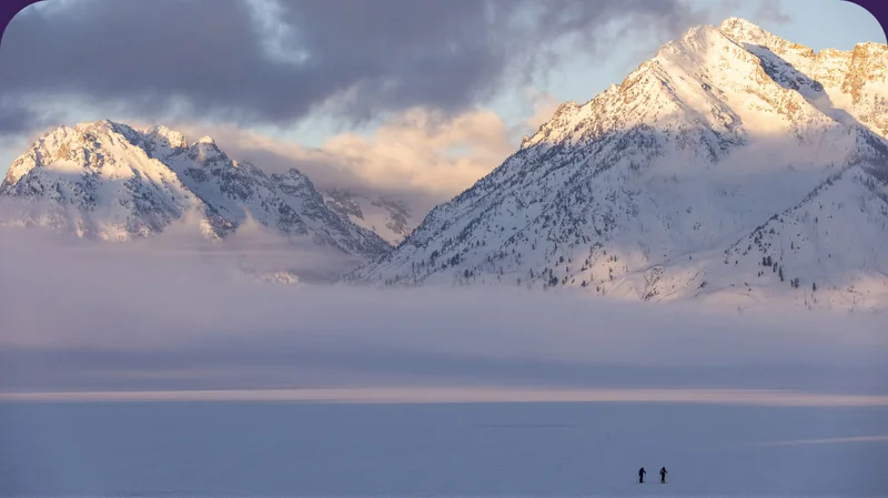 Two skiers traverse a snowy mountain valley.