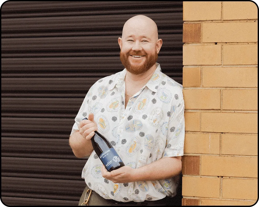 Bodie wears a poppy shirt while holding Domaine Bertrand's Pinot.