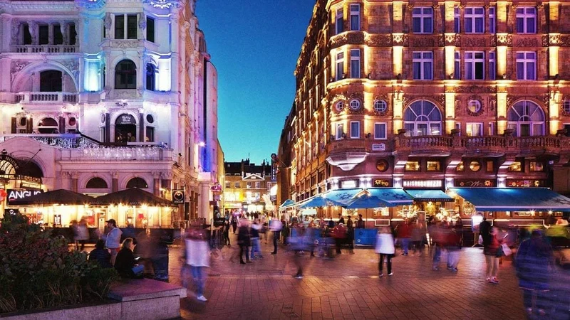 Image description: Motion blur people move about square at night in London.