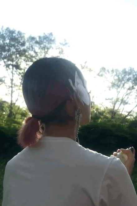 A person with a shirt ponytail sprays toner on their face with their back to the camera