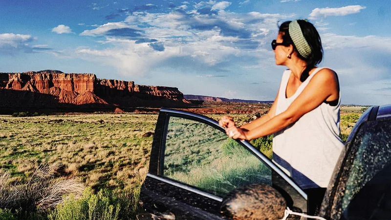 Image description: Woman standing next to open car door viewing desert landscape in Utah