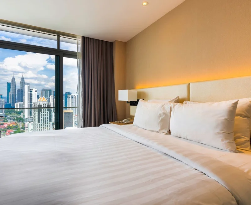 Image description: Hotel room with a large white bed and city skyline views out the window.