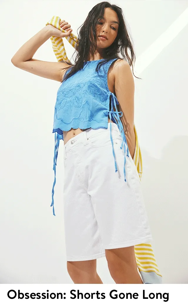 Woman wearing a floral-embroidered top and knee-length white denim shorts.