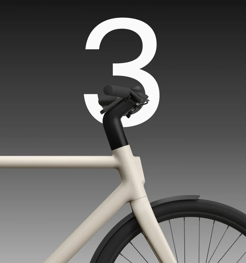 A close-up side profile of a Cowboy bike in a neutral sand colour. The handlebars and top of the front wheel are prominent, set against a gradient background with a large white numeral “3” in the centre.