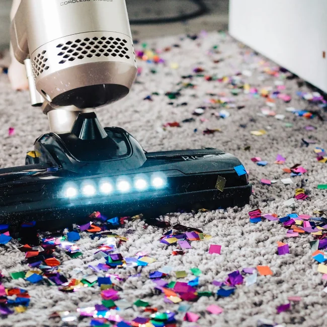 A vacuum cleaner is picking up multicolored bits of paper off a carpet.
