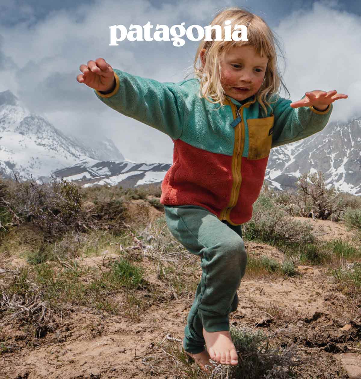 Patagonia. A barefoot child jumping on rocks in the desert below huge snowy mountains.