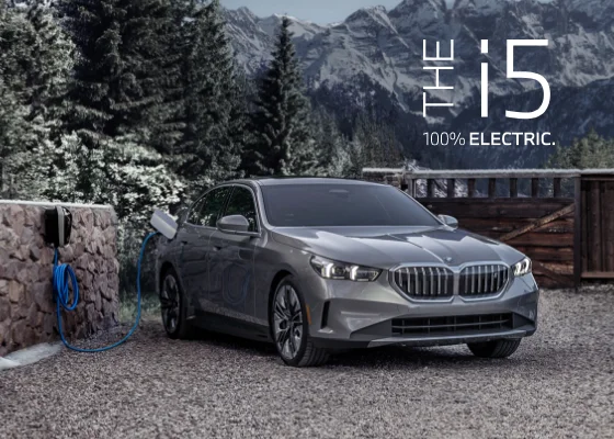 The BMW i5 parked in front of snow covered trees with mountains in the back. The i5. 100% Electric.