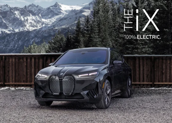 The BMW iX parked in front of snow covered trees with mountains in the back. The iX. 100% Electric.