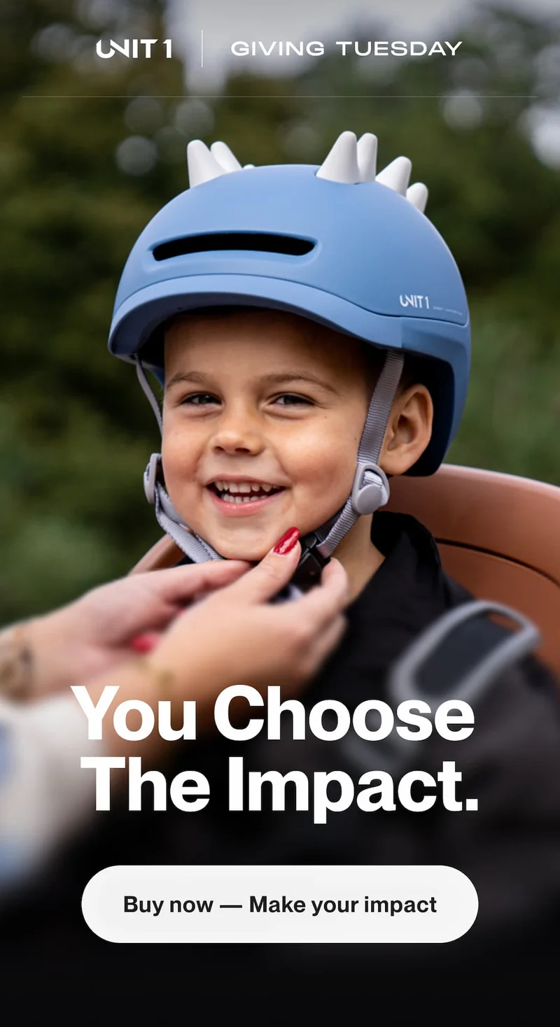 Smiling child wearing a blue UNIT 1 SPARKY helmet while a parent adjusts the strap during Giving Tuesday.